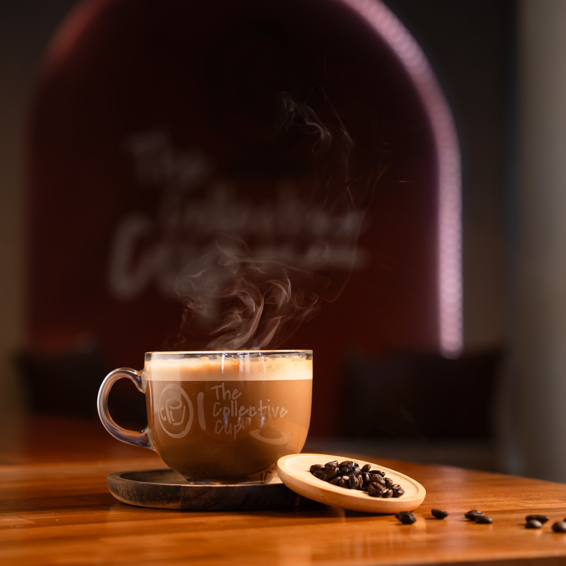 Close-up of a steaming glass mug of coffee with roasted beans on a wooden coaster