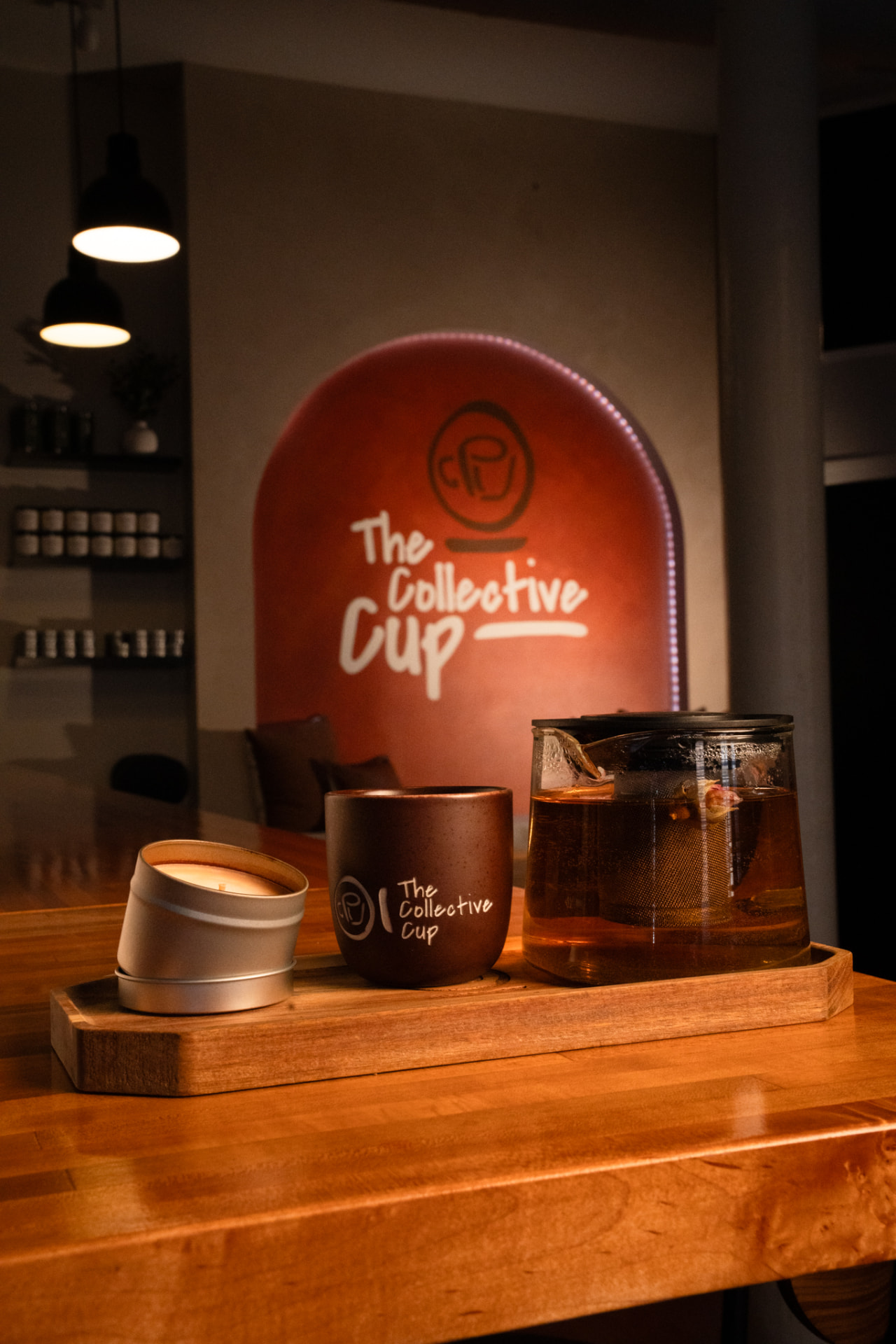 A glass teapot of amber tea and a branded ceramic cup arranged on a wooden tray