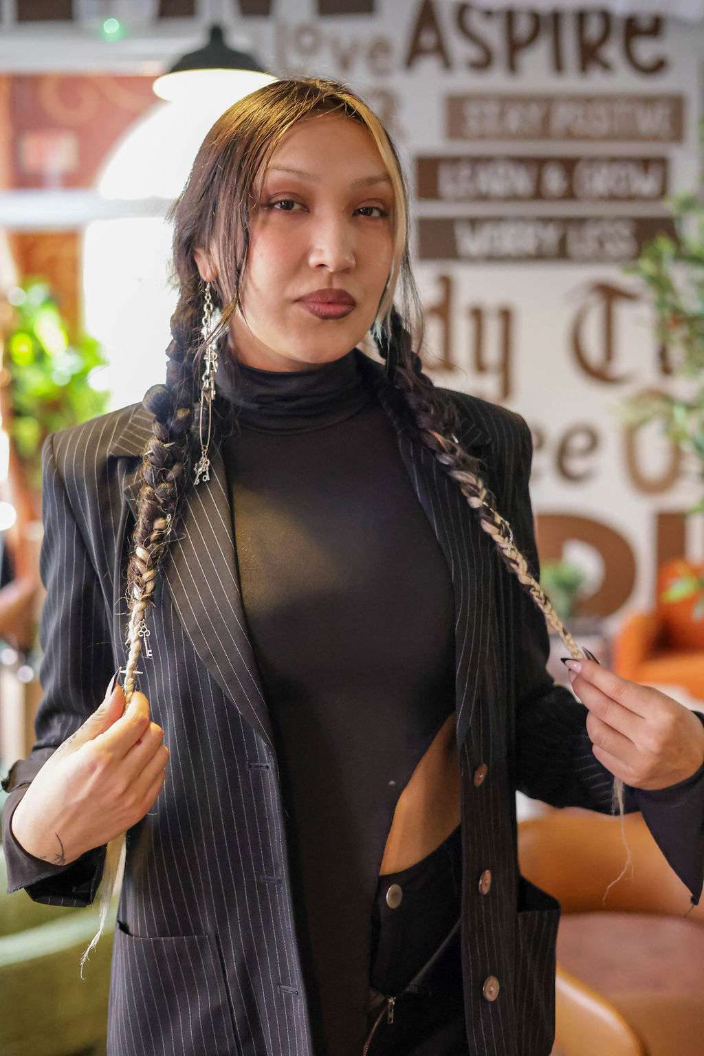 A guest with long braids accented by silver chains posing in front of the wall art reading Stay Positive and Learn & Grow