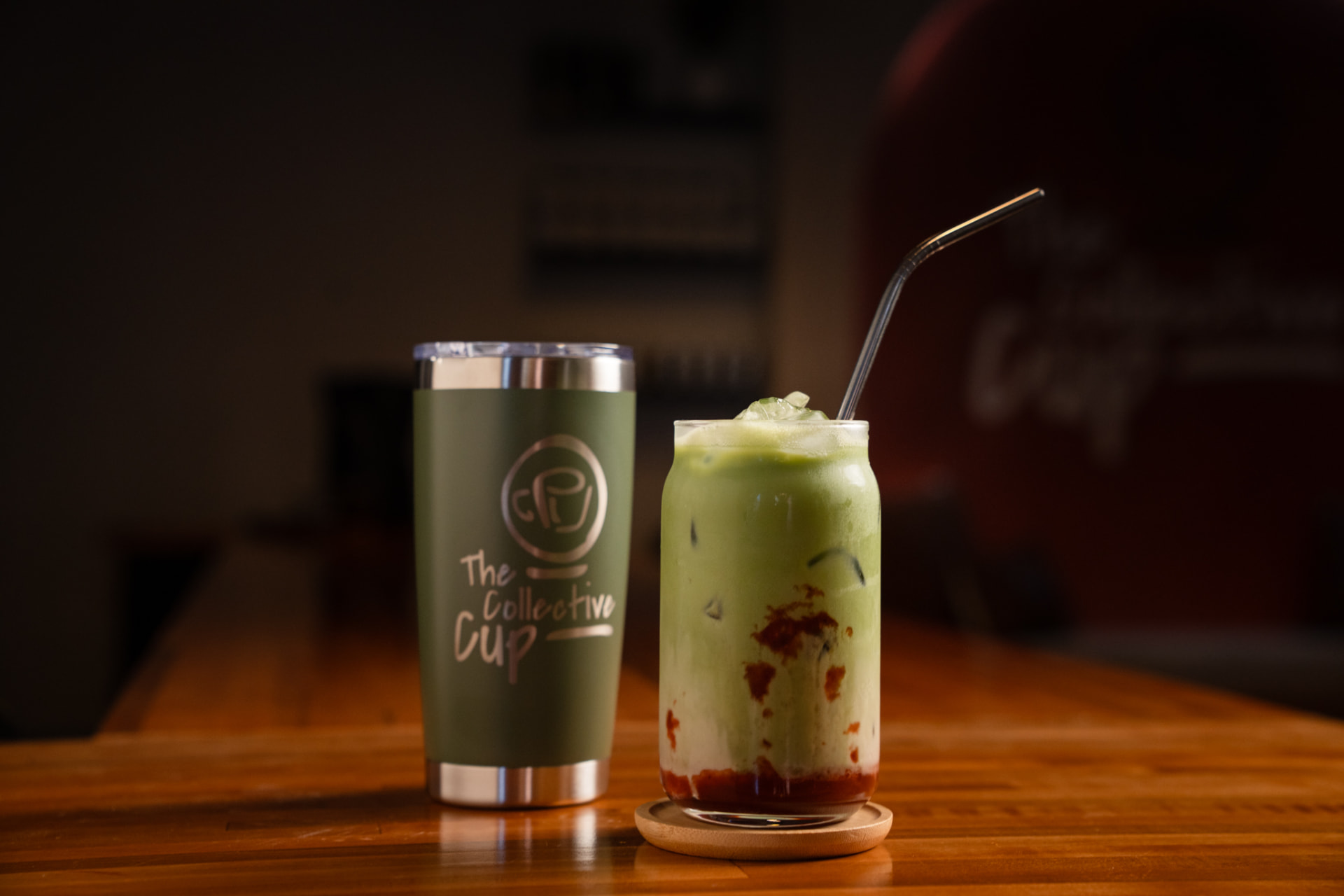 An iced layered matcha drink beside an olive-green branded tumbler