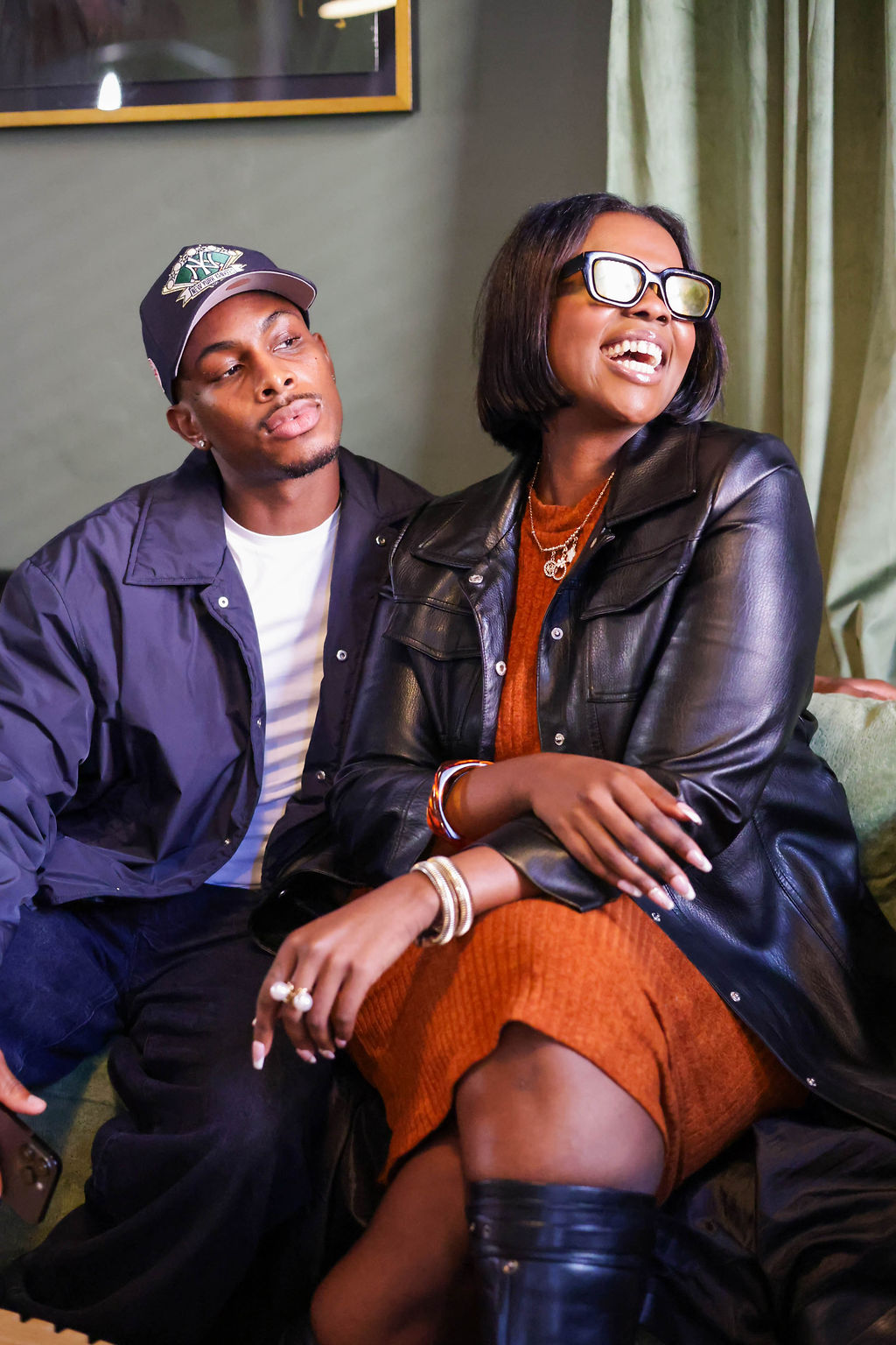 Two guests laughing together on the sage green sofa