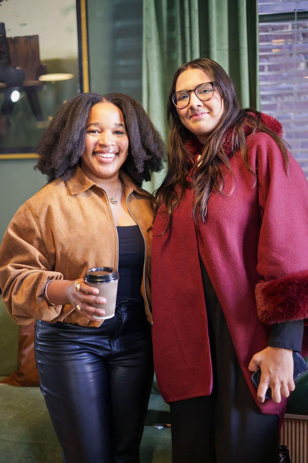 Two guests posing together with a coffee cup, one in a burgundy coat